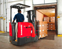 A forklift operator drives into a docked trailer with a pallet of boxes.